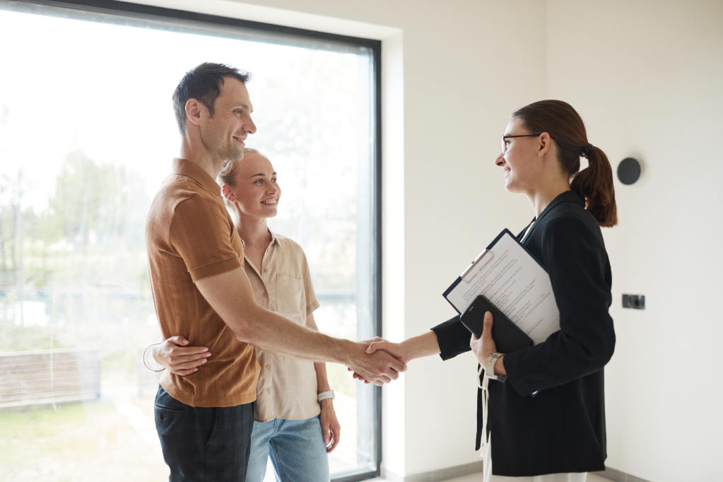 Side view portrait of young couple shaking hands with real estate agent during apartment tour, copy space